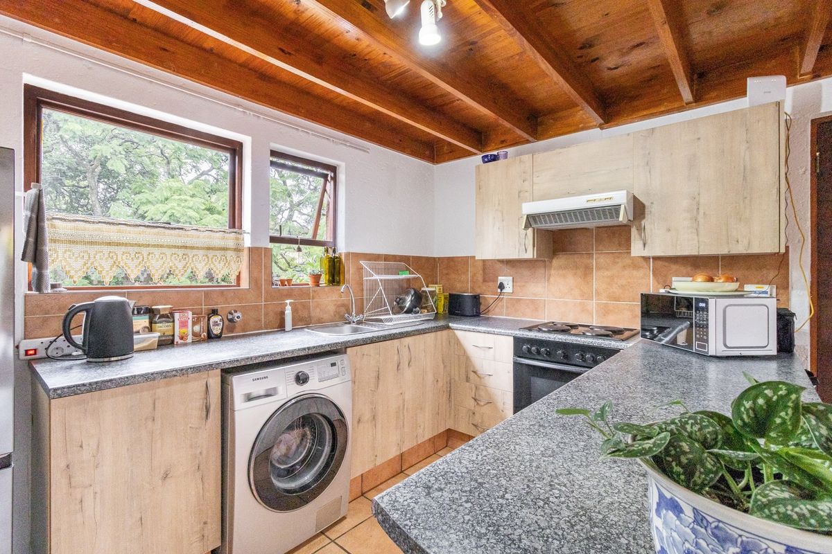Functional kitchen featuring light wood-finish cabinetry, granite-look countertops, built-in oven with extractor, and exposed timber ceiling beams, providing a warm, practical workspace.