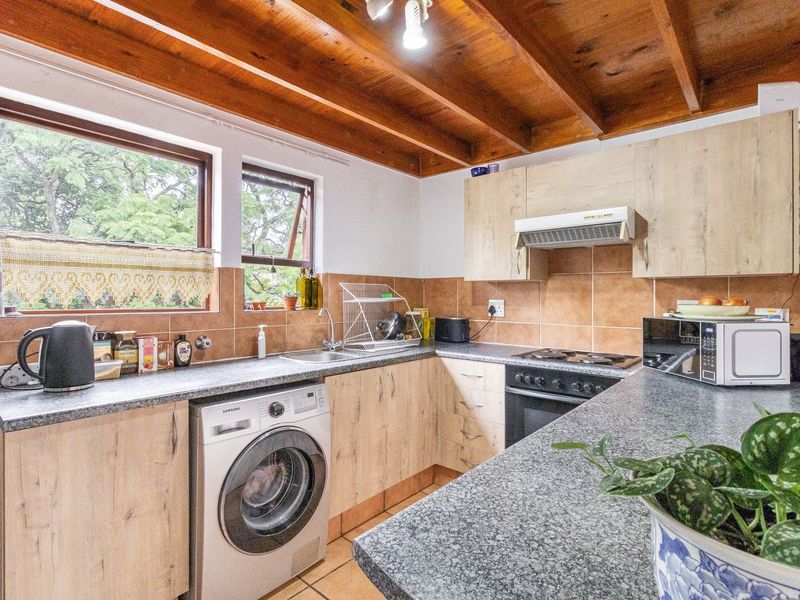 Functional kitchen featuring light wood-finish cabinetry, granite-look countertops, built-in oven with extractor, and exposed timber ceiling beams, providing a warm, practical workspace.