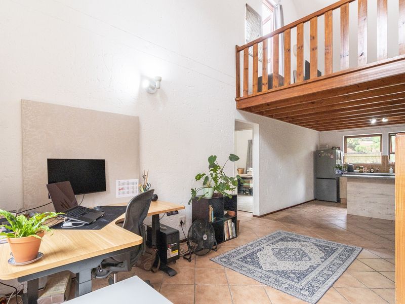 Open plan living area featuring a mezzanine level with wooden balustrade, tiled flooring, and an integrated kitchen space.