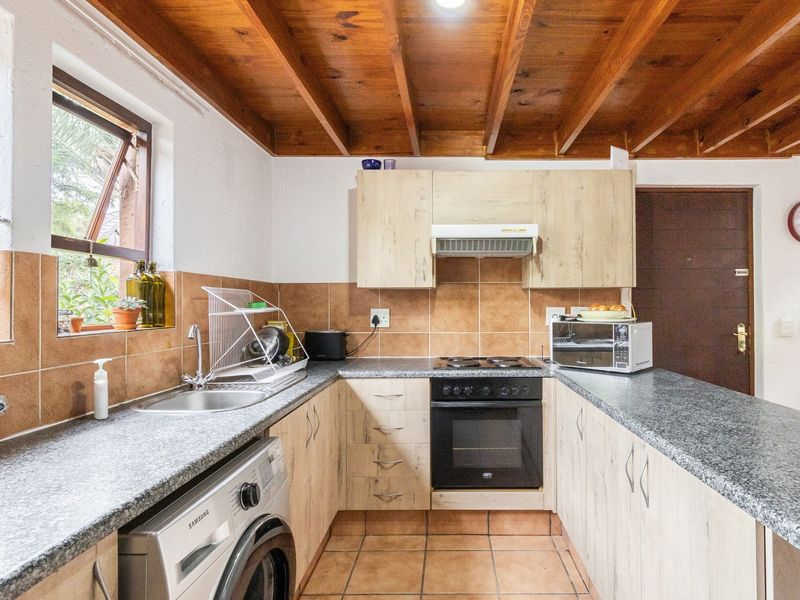 Functional kitchen featuring light wood cabinetry, granite countertops, built-in oven, hob, extractor fan, and a distinctive exposed timber beam ceiling.