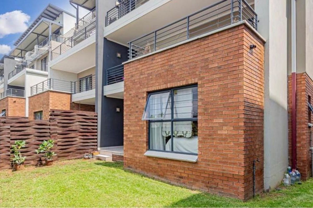 Rear view of the apartment building featuring a face brick facade, private patio area, and metal balcony railings overlooking a small garden space.