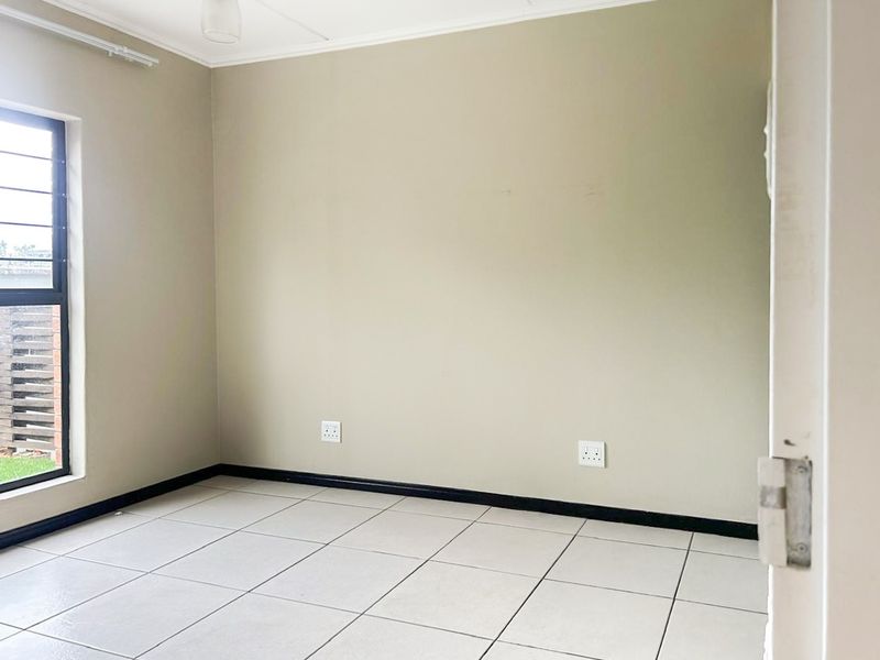 An empty bedroom featuring neutral wall paint, tiled flooring, and a window fitted with security burglar bars.