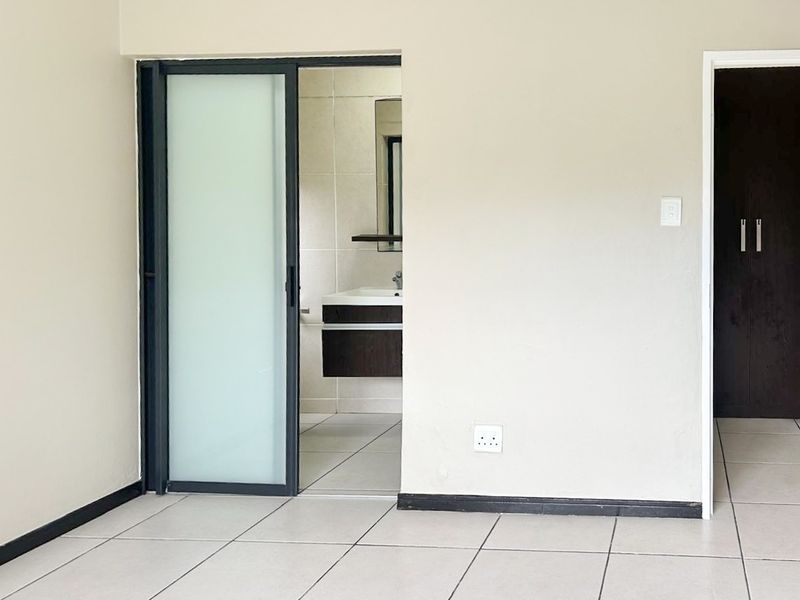 A bright, empty bedroom featuring tiled floors, a modern sliding frosted glass door leading to an en-suite bathroom, and a built-in cupboard.