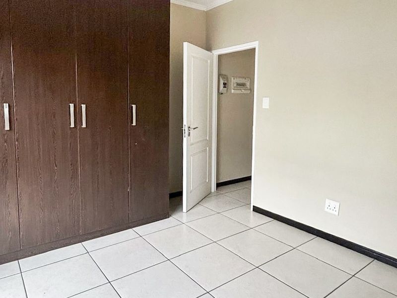 A clean, empty bedroom featuring neutral tiled flooring, built-in dark wood cupboards, and a simple pendant light fixture.