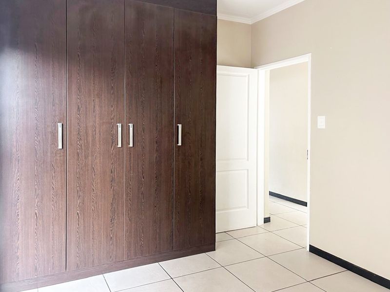 A clean, empty bedroom featuring dark wood built-in cupboards, neutral wall finishes, and light-colored floor tiles.