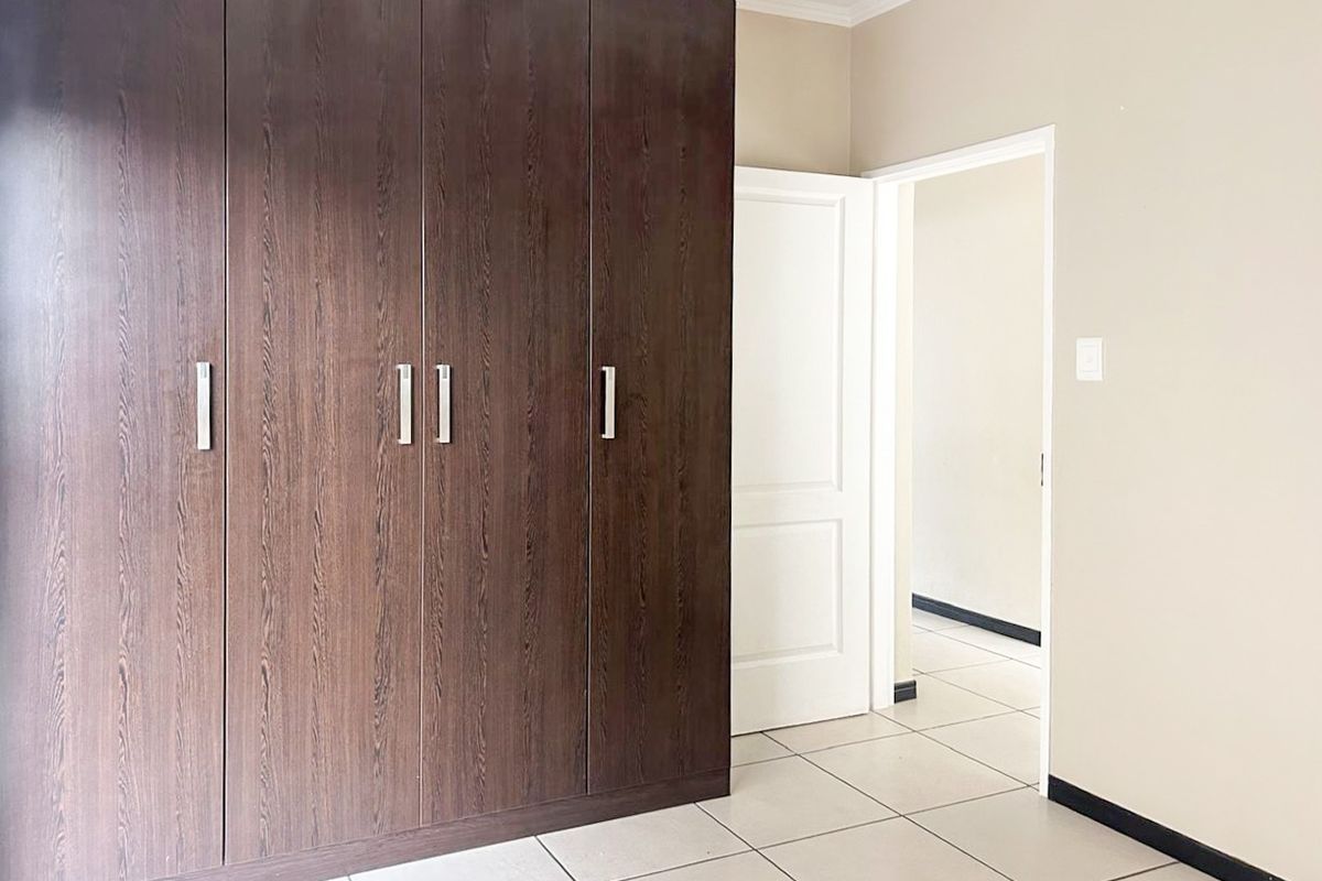 A clean, empty bedroom featuring dark wood built-in cupboards, neutral wall finishes, and light-colored floor tiles.