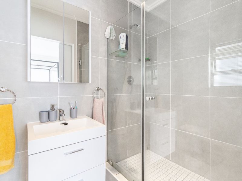 Modern bathroom featuring a sleek vanity with basin, mirrored medicine cabinet, and a spacious walk-in shower with glass screen and neutral wall tiling.
