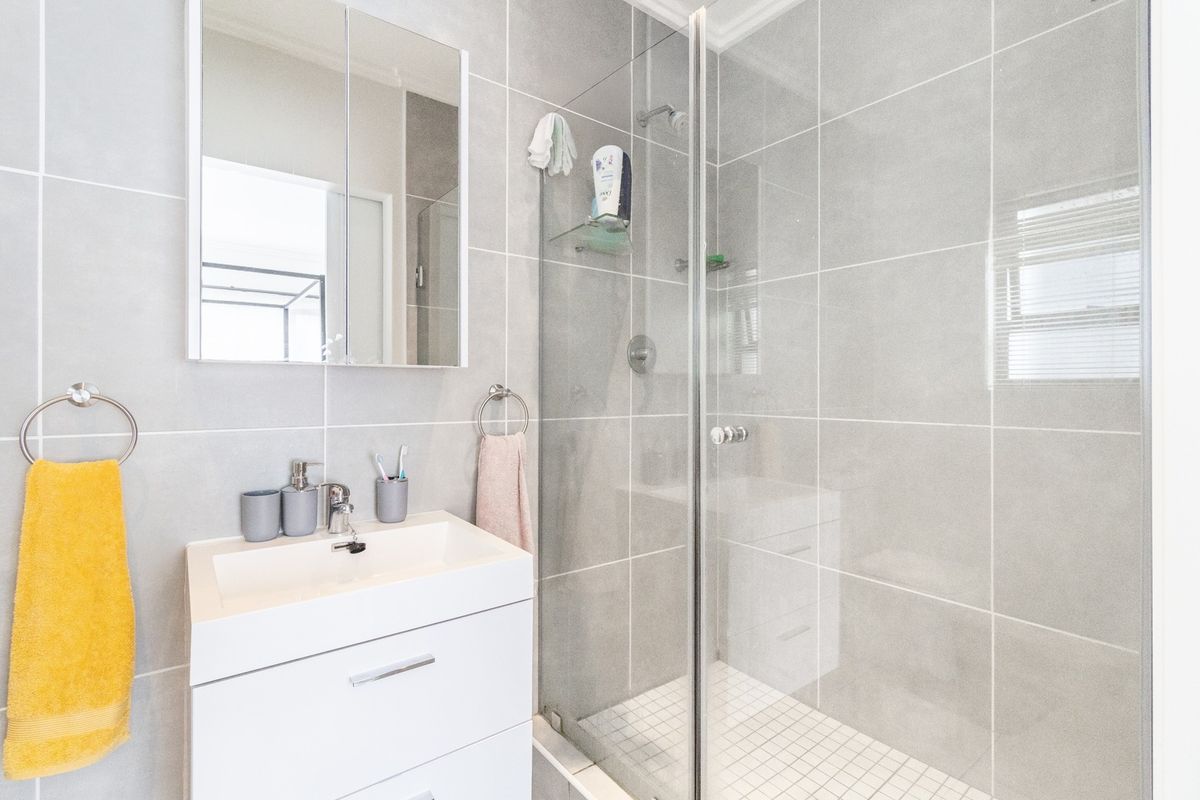 Modern bathroom featuring a sleek vanity with basin, mirrored medicine cabinet, and a spacious walk-in shower with glass screen and neutral wall tiling.