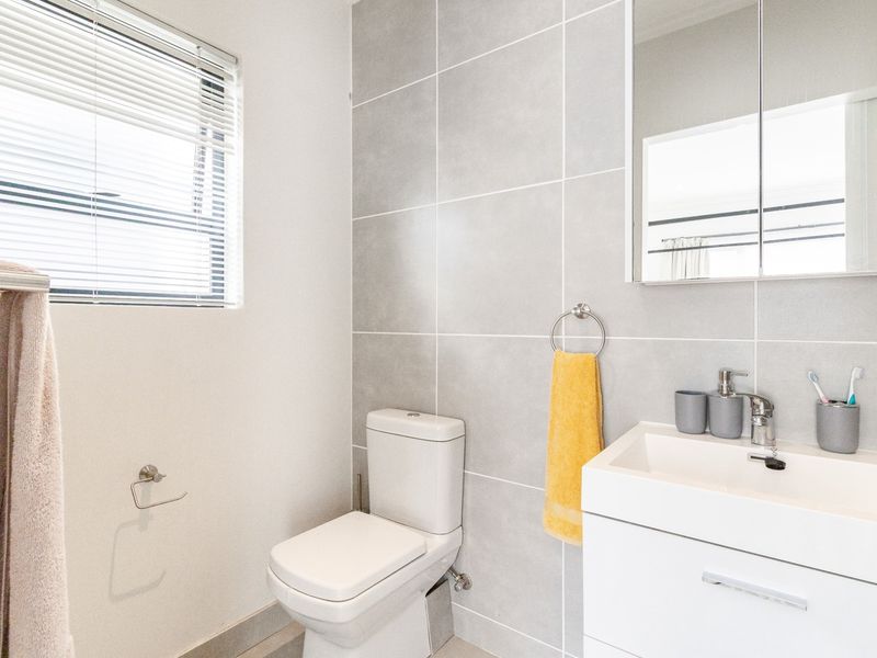 A modern, well-maintained bathroom featuring a sleek vanity cabinet, basin with mixer tap, toilet, and neutral grey wall tiling.