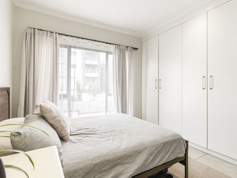 A bright and well-maintained bedroom featuring floor-to-ceiling built-in cupboards, neutral tiled flooring, and a large window allowing for ample natural light.