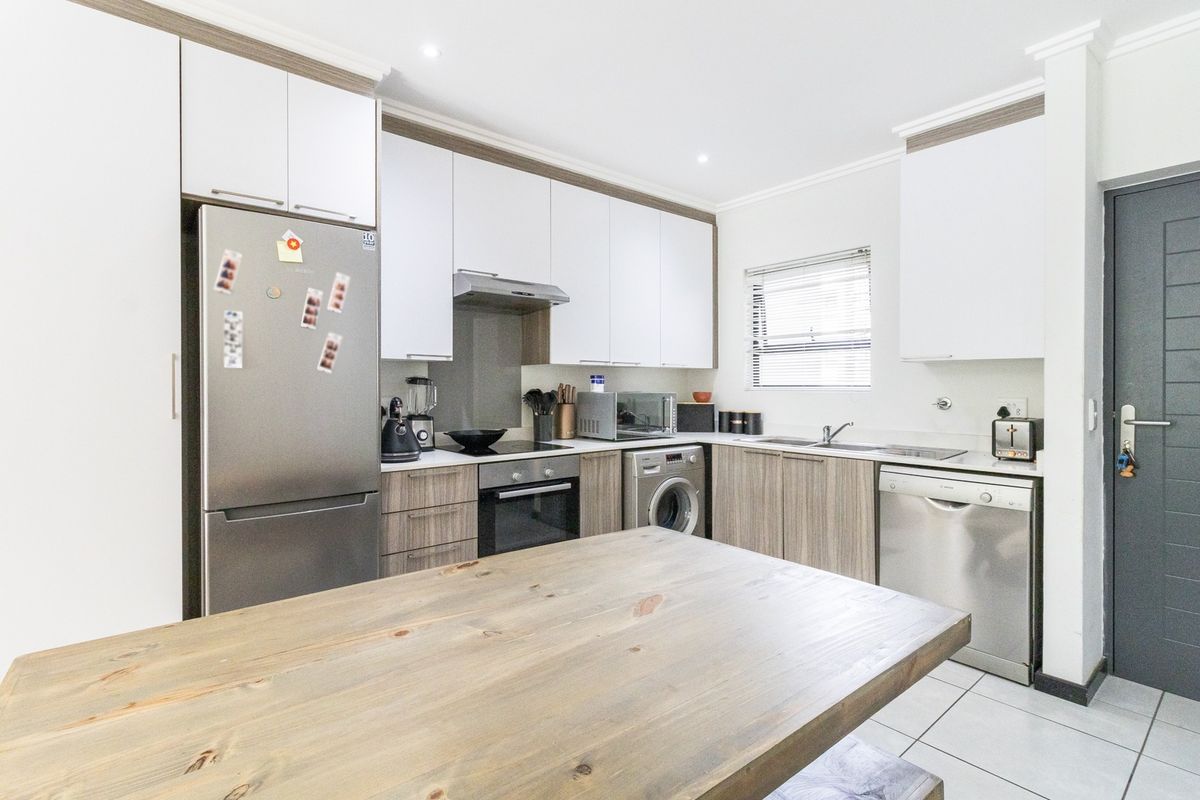 Modern kitchen featuring sleek white and wood-grain cabinetry, integrated appliances, tiled flooring, and a functional layout with ample counter space.