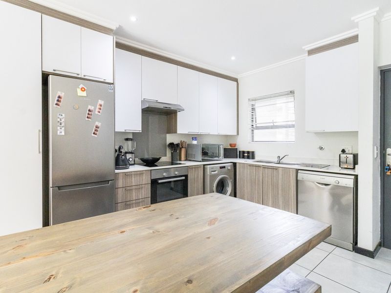 Modern kitchen featuring sleek white and wood-grain cabinetry, integrated appliances, tiled flooring, and a functional layout with ample counter space.
