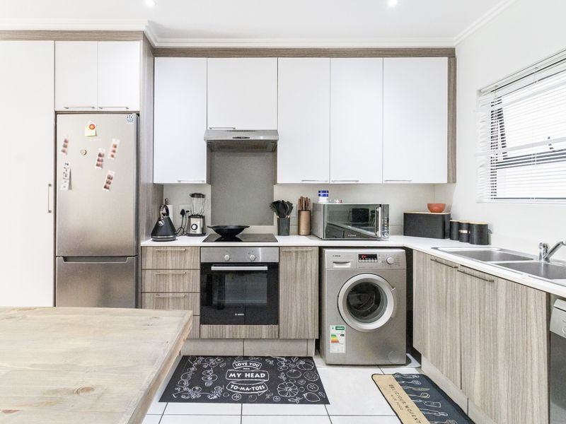 Modern kitchen featuring sleek two-tone cabinetry, integrated appliances, electric hob, oven, and a stainless steel sink with tiled flooring.