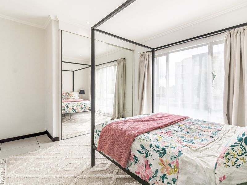 A bright and well-maintained bedroom featuring large windows, tiled flooring, and a spacious built-in mirror wardrobe.