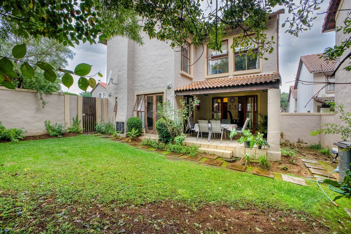 Rear view of the house featuring a covered patio area, established garden, and boundary walls, providing a private outdoor space for relaxation.
