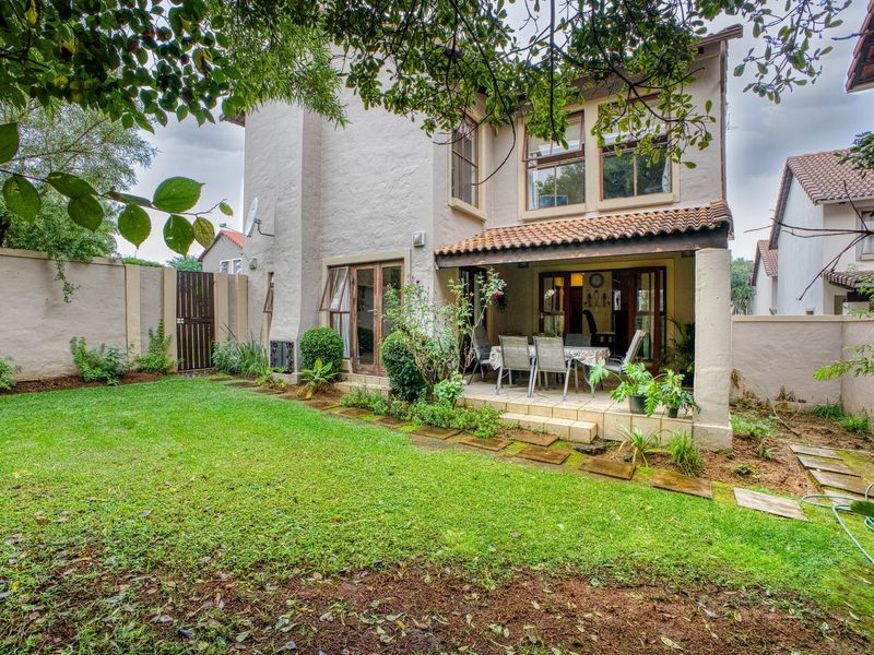 Rear view of the house featuring a covered patio area, established garden, and boundary walls, providing a private outdoor space for relaxation.