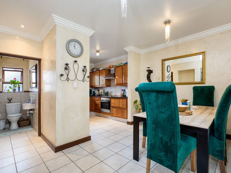 Open-plan dining area adjacent to a functional kitchen with wooden cabinetry and a separate guest bathroom featuring tiled finishes.