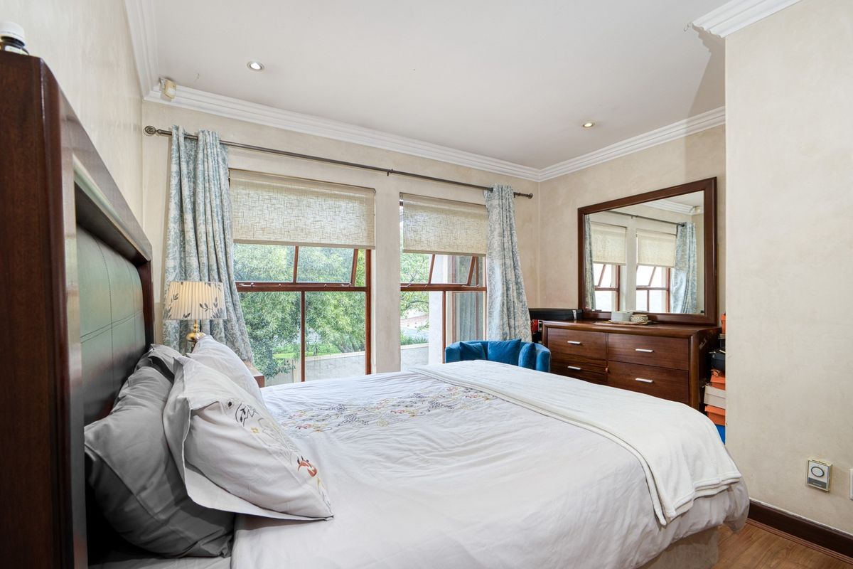 A well-maintained bedroom featuring timber-framed windows, recessed downlighting, crown molding, and laminate flooring, offering a comfortable and bright living space.