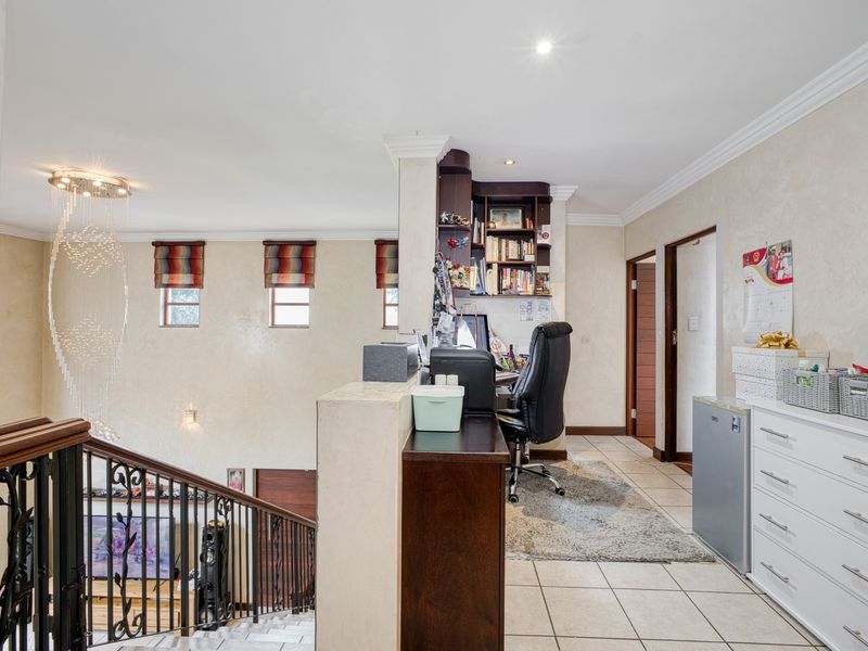 A functional home office area featuring built-in shelving, tiled flooring, and an open-plan layout overlooking the staircase with decorative chandelier lighting.