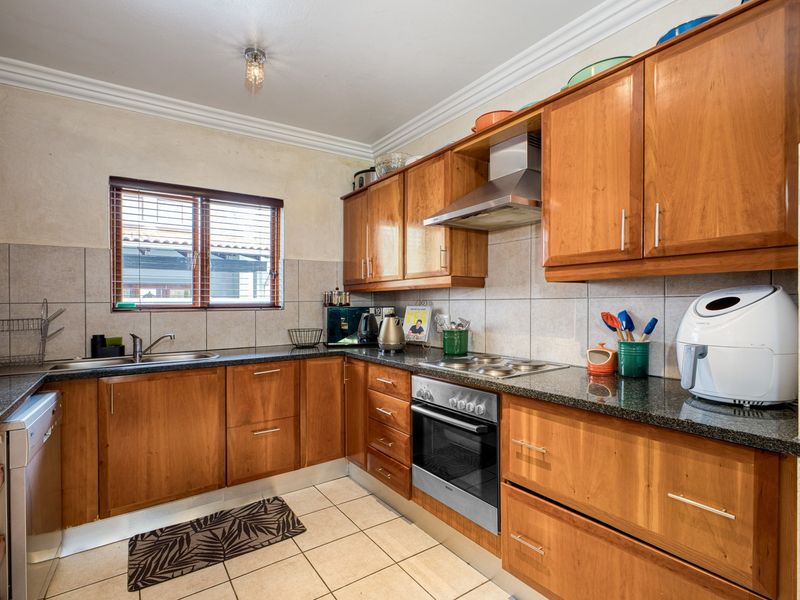 A functional kitchen featuring wooden cabinetry, granite countertops, and integrated stainless steel appliances, complemented by tiled flooring and a tiled backsplash.