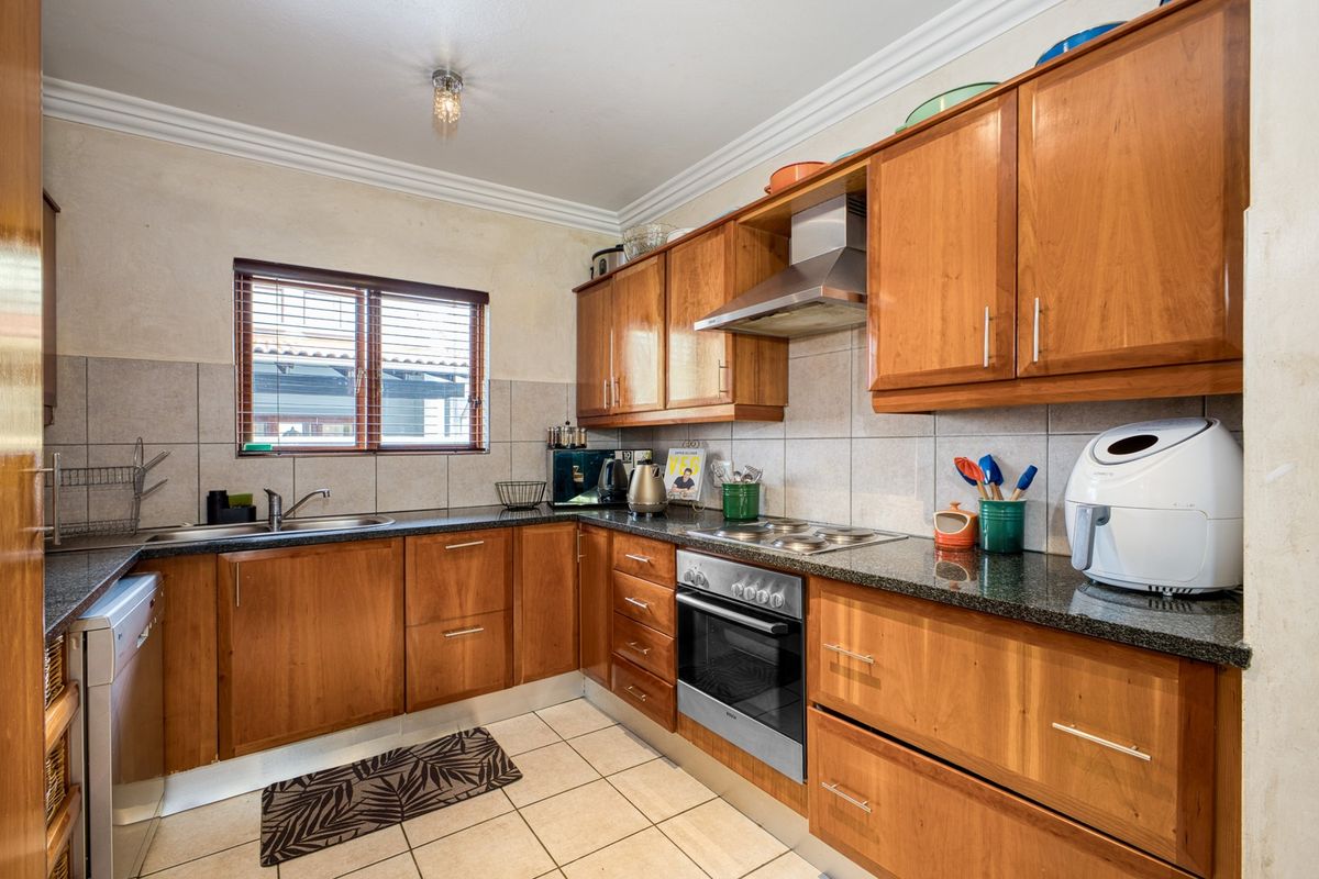 A functional kitchen featuring wooden cabinetry, granite countertops, and integrated stainless steel appliances, complemented by tiled flooring and a tiled backsplash.