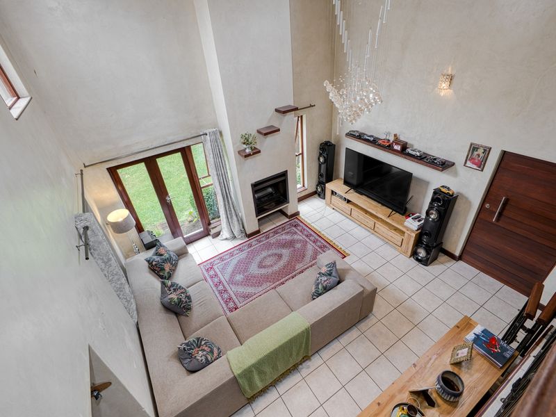 Spacious double-volume living room featuring tiled floors, a built-in fireplace, and direct access to the garden through glass french doors.