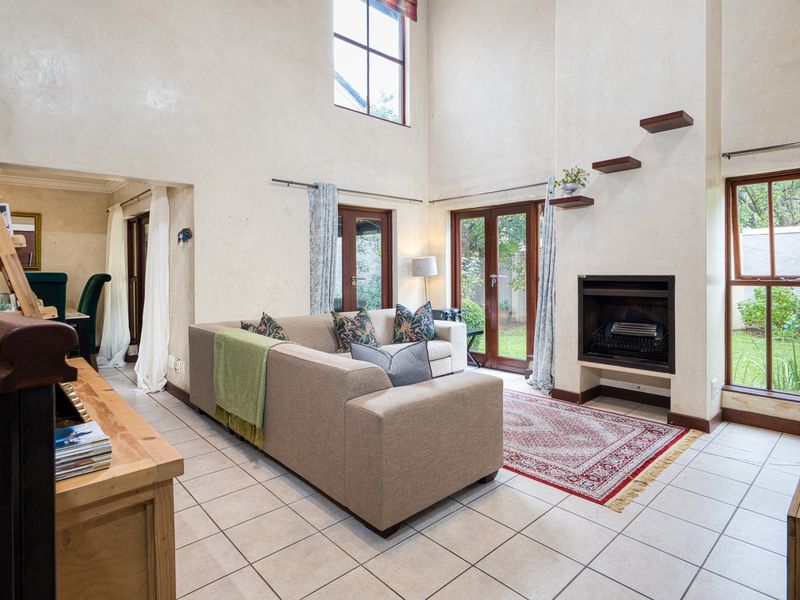Spacious living room featuring double volume ceilings, a built-in fireplace, tiled flooring, and direct access to the garden through french doors.