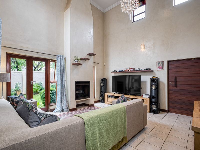 Spacious living room featuring a double-height ceiling, a central fireplace, tiled flooring, and direct access to the garden through wooden french doors.