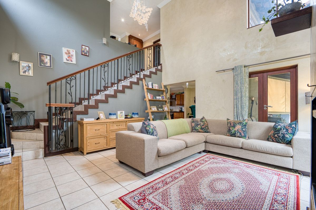 Spacious double-volume living room featuring tiled flooring, a decorative wrought iron staircase, and direct access to the outdoor area through french doors.