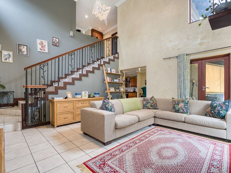 Spacious double-volume living room featuring tiled flooring, a decorative wrought iron staircase, and direct access to the outdoor area through french doors.