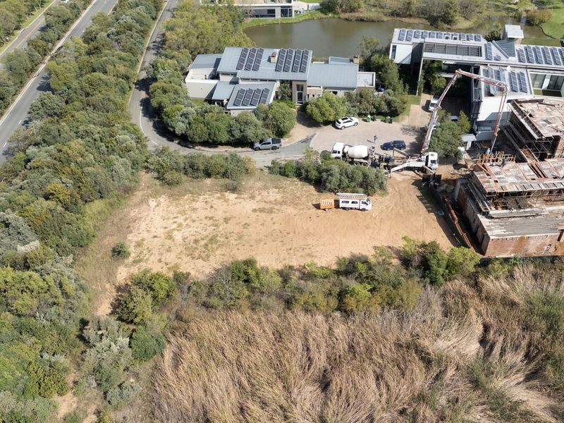 Aerial view of a vacant residential plot situated next to an active construction site and established estate greenery.