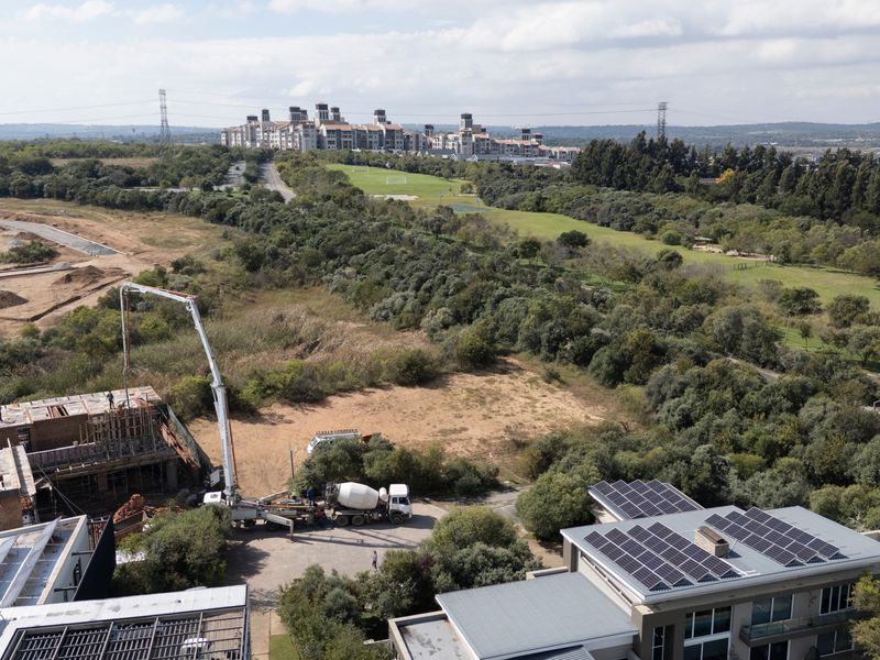 Aerial view of a residential development site featuring active construction, concrete pumping equipment, and surrounding natural landscape with nearby established properties.