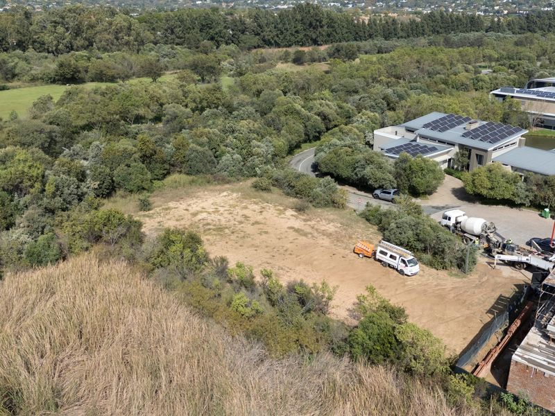Aerial view of a vacant residential plot surrounded by established trees and greenery, adjacent to an existing residential development.