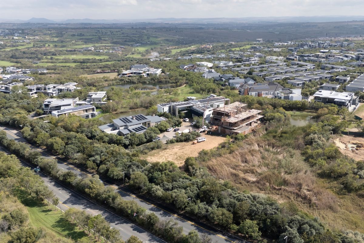 An aerial view of a residential estate featuring established homes, natural landscaping, water features, and surrounding road infrastructure.