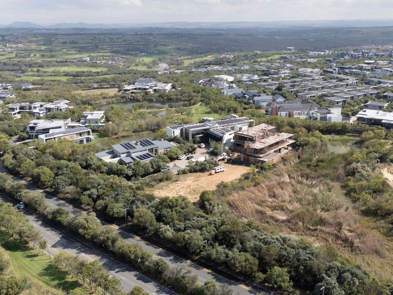 An aerial view of a residential estate featuring established homes, natural landscaping, water features, and surrounding road infrastructure.