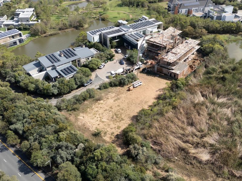 Aerial view of a vacant residential plot situated within a developed estate, featuring surrounding natural landscape and nearby ongoing construction.