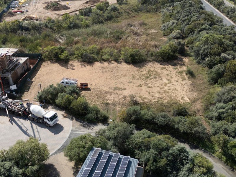 Aerial view of a vacant residential plot featuring surrounding vegetation, a paved driveway, and adjacent construction activity.