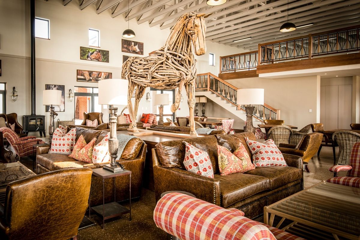 Spacious open-plan living area featuring high exposed timber ceilings, polished concrete floors, a wood-burning fireplace, and a mezzanine level with a decorative staircase.