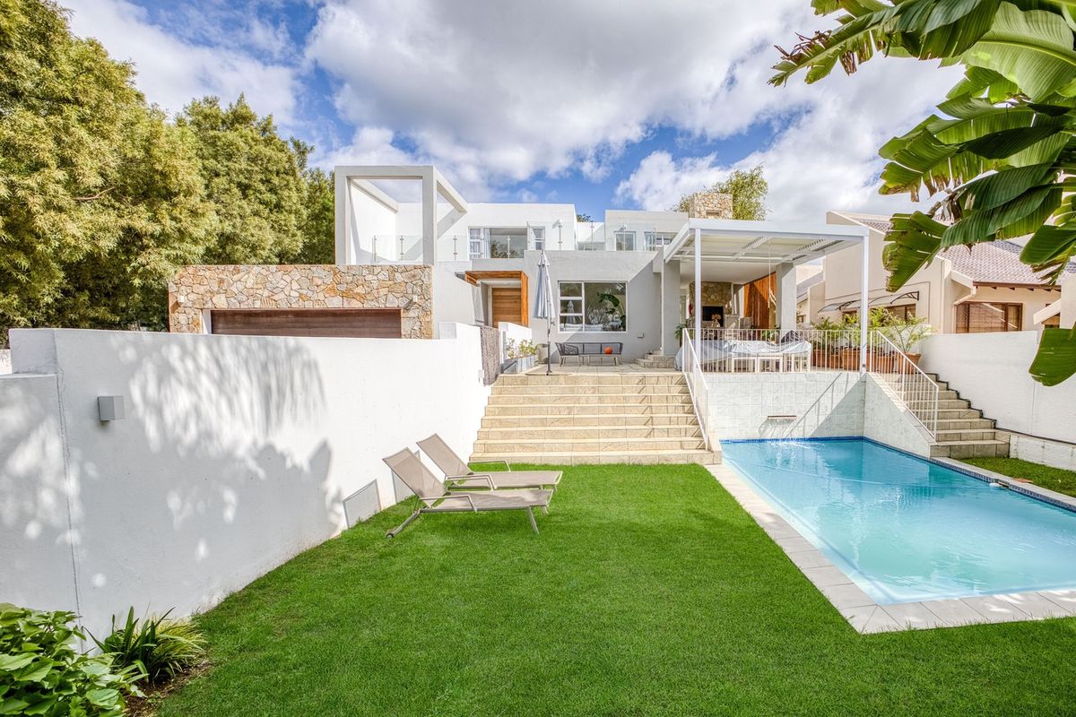 Rear view of a modern multi-level home featuring a swimming pool, landscaped lawn, stone-clad facade, and a covered patio area with an outdoor fireplace.