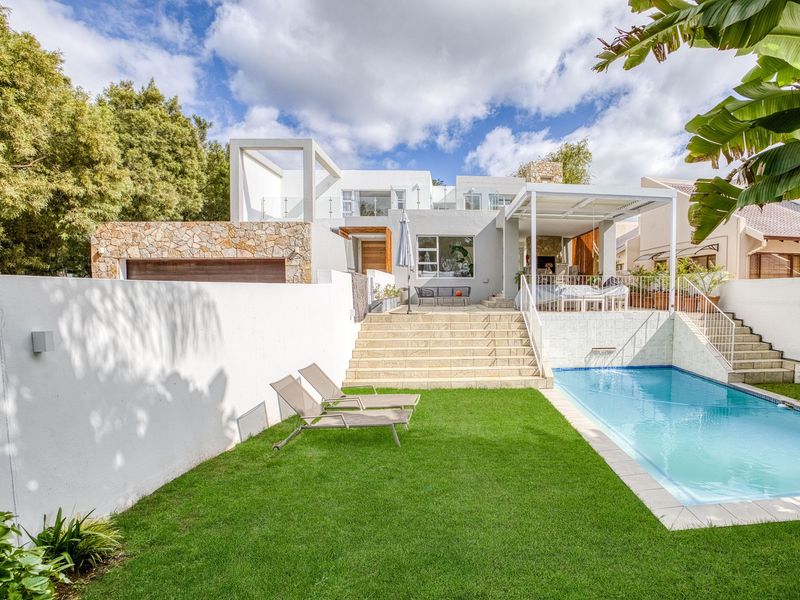 Rear view of a modern multi-level home featuring a swimming pool, landscaped lawn, stone-clad facade, and a covered patio area with an outdoor fireplace.