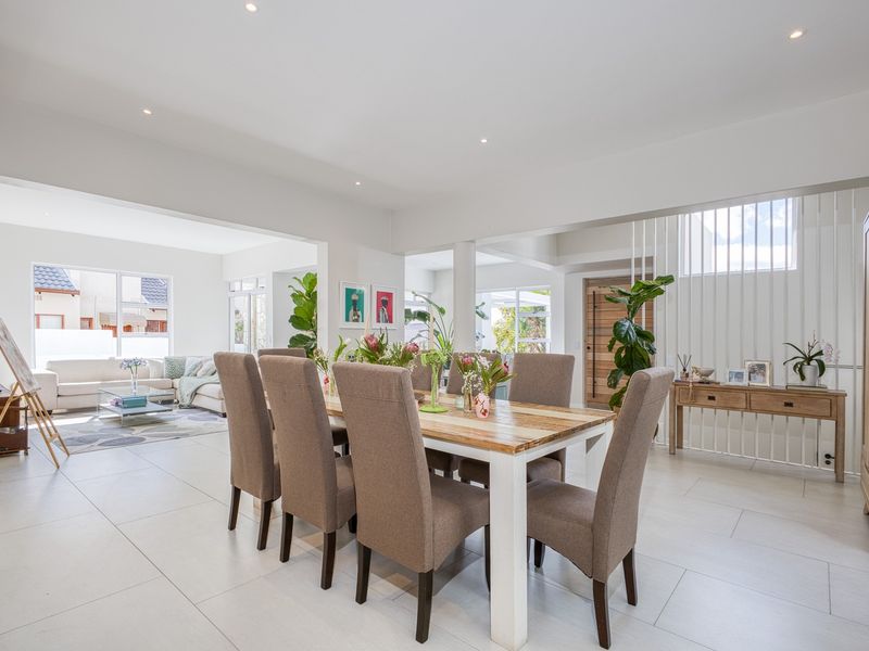 Spacious open-plan living and dining area featuring neutral tiled flooring, recessed lighting, and a modern vertical slat feature wall near the entrance.