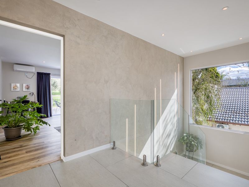 Modern hallway featuring a sleek glass balustrade, textured wall finish, and large window providing natural light and views.