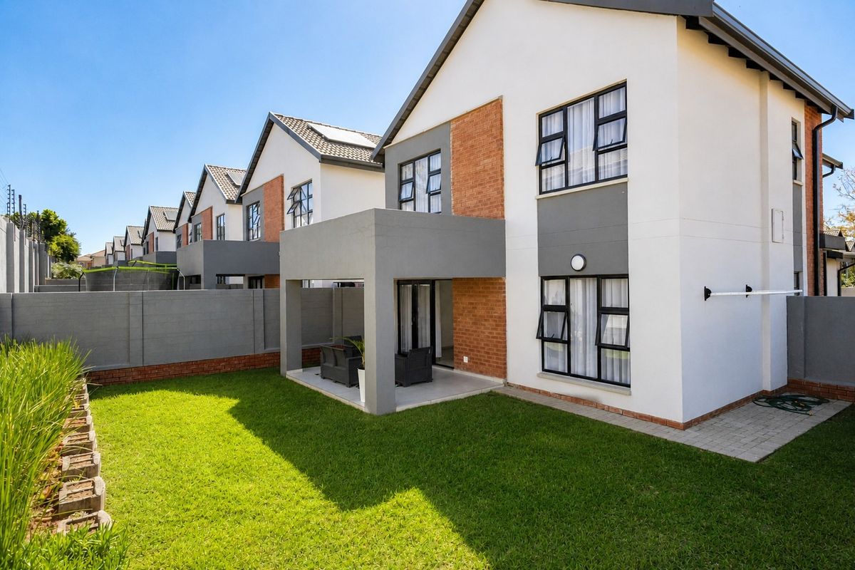 Rear view of a modern townhouse featuring a covered patio, private garden, and well-maintained brick and plaster exterior finishes.