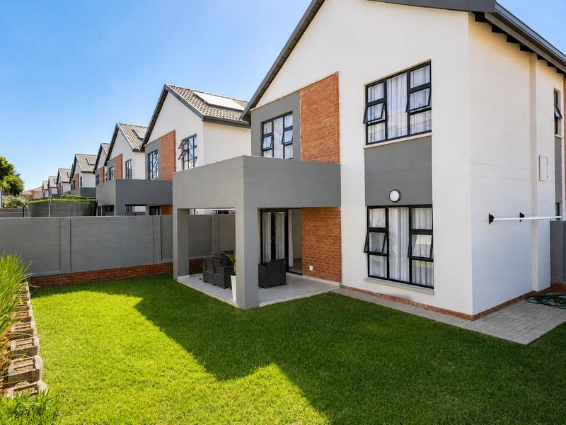 Rear view of a modern townhouse featuring a covered patio, private garden, and well-maintained brick and plaster exterior finishes.