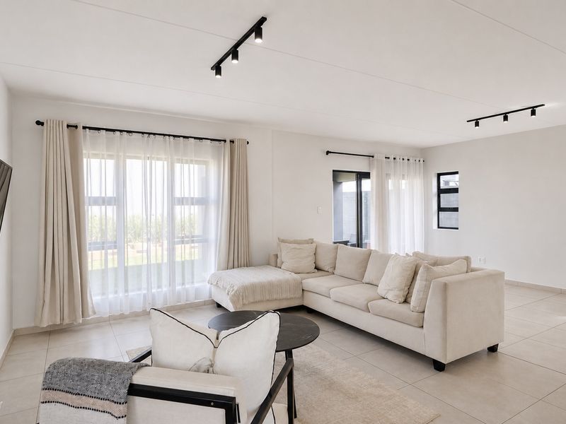 A bright and modern living room featuring neutral tiled flooring, contemporary track lighting, and large windows that provide ample natural light.