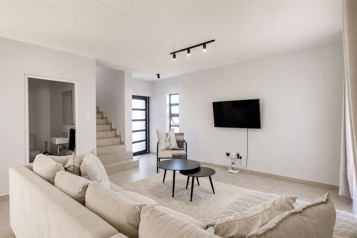 Modern open-plan living area featuring neutral tiled flooring, contemporary track lighting, and direct access to a staircase and guest bathroom.