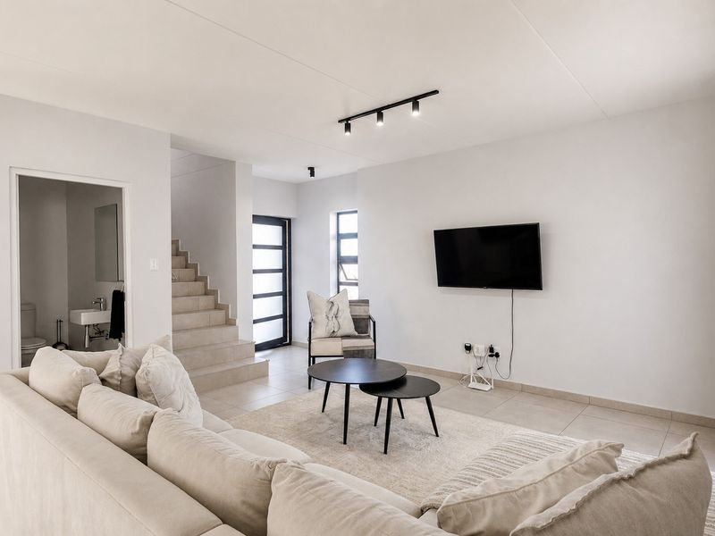 Modern open-plan living area featuring neutral tiled flooring, contemporary track lighting, and direct access to a staircase and guest bathroom.