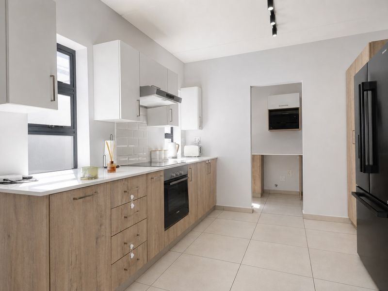 Modern kitchen featuring light wood-tone cabinetry, stone countertops, subway tile backsplash, integrated oven and hob, and sleek track lighting.