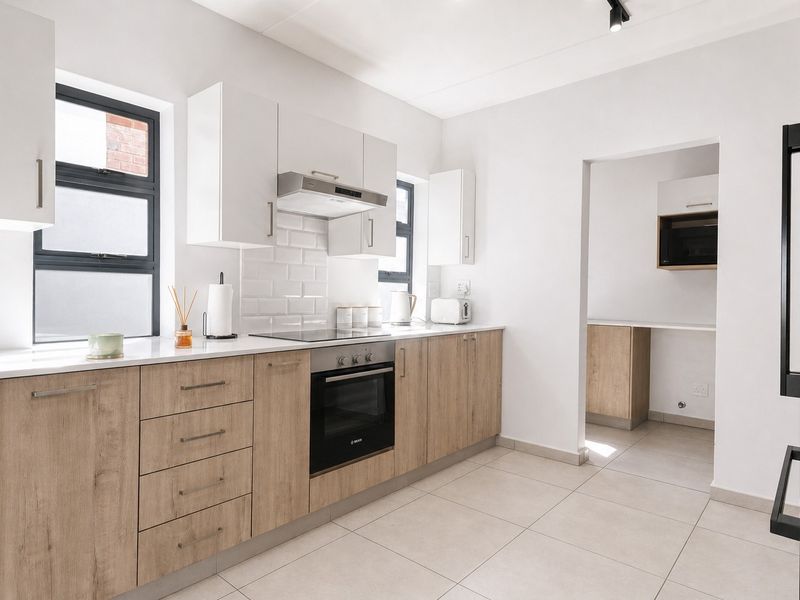 Modern kitchen featuring light wood-finish cabinetry, stone countertops, subway tile backsplash, and integrated appliances, with an adjacent scullery area.