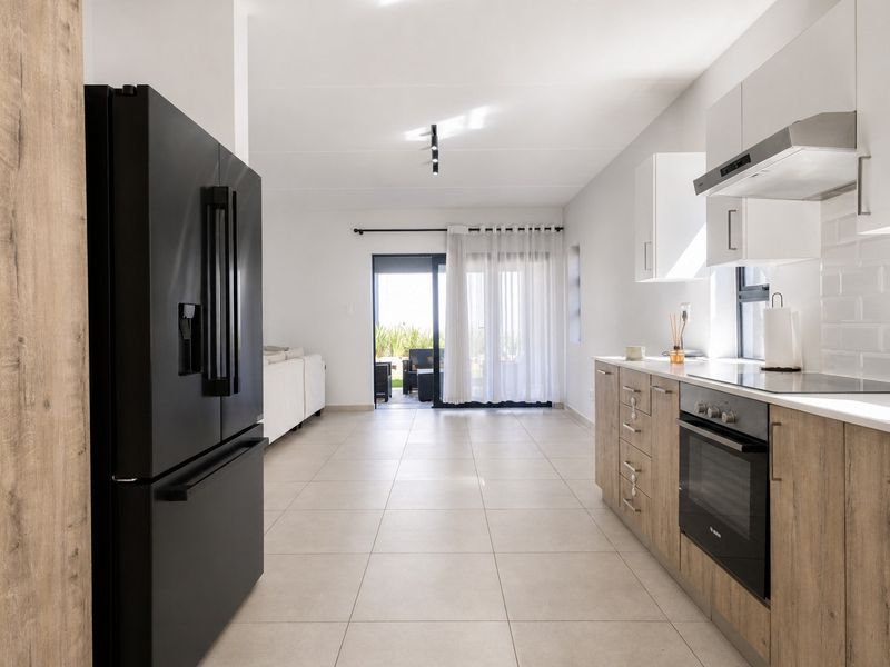 Modern open-plan kitchen featuring wood-finish cabinetry, integrated appliances, and subway tile backsplash, flowing seamlessly into the living area with access to the patio.